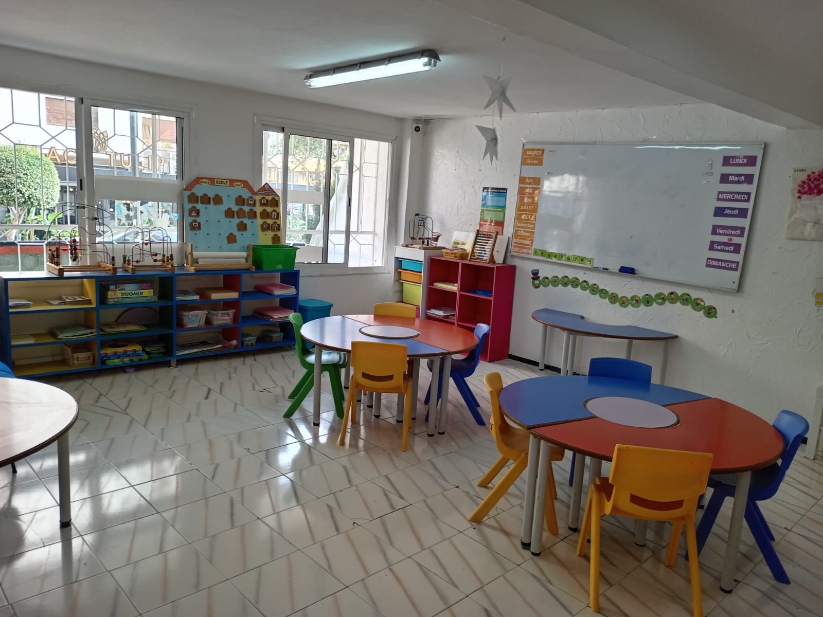 Salle d'éveil lumineuse avec tables colorées et étagères de jeux éducatifs